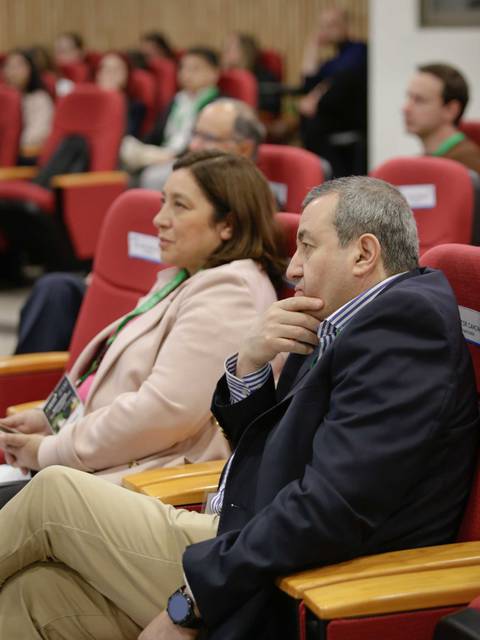 Dos personas pensativas en un evento con público sentado detrás.
