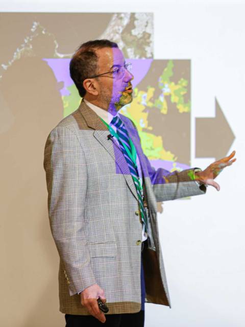 Un hombre presenta información en una diapositiva mientras señala hacia una imagen proyectada.