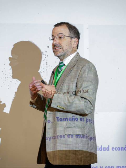 Un hombre disertando frente a una presentación en un evento académico.