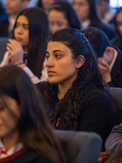 Un grupo de estudiantes escucha atentamente durante un evento en un salón.