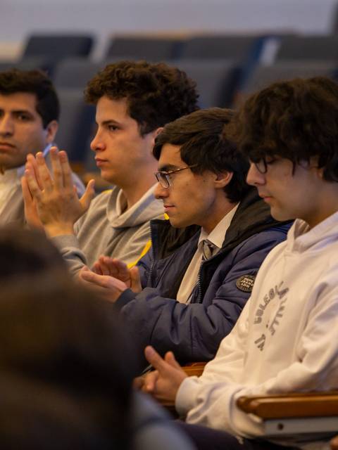 Un grupo de jóvenes sentados en un auditorio, algunos aplaudiendo y otros escuchando atentamente.