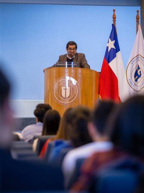 Un orador habla desde un podio frente a un público en un evento institucional.