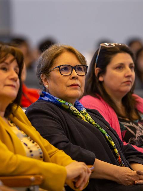 Un grupo de mujeres sentadas en un evento, escuchando atentamente.