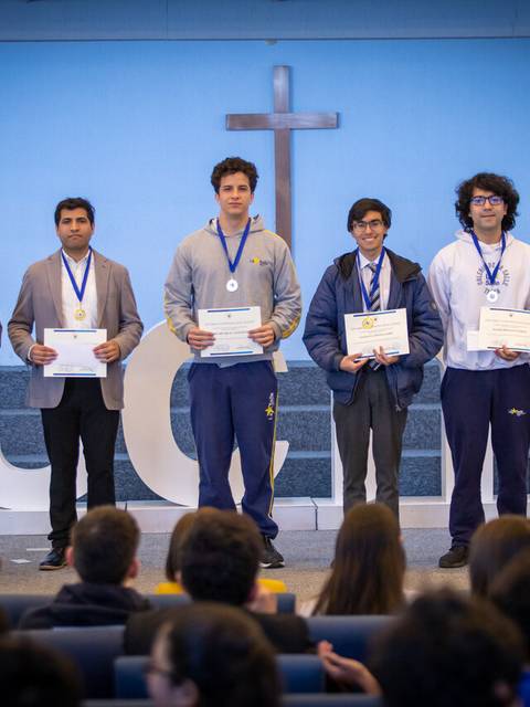 Estudiantes en un escenario sosteniendo diplomas y medallas durante una ceremonia de premiación.