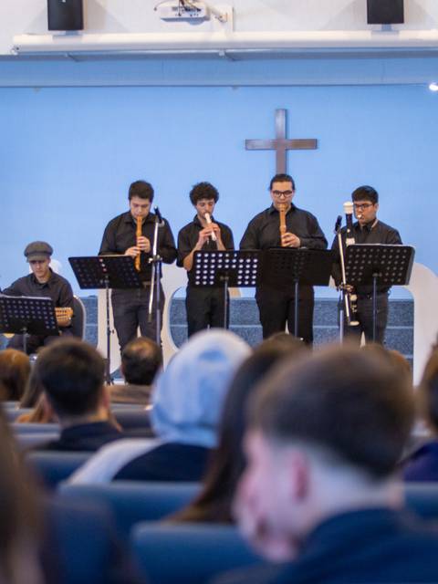 Un grupo de jóvenes músicos toca instrumentos de viento en una iglesia durante un evento.