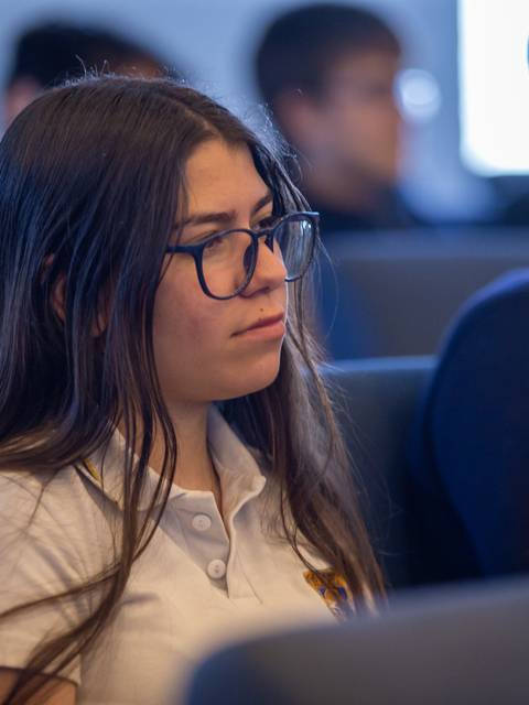 Una joven con gafas escucha atentamente en un auditorio.