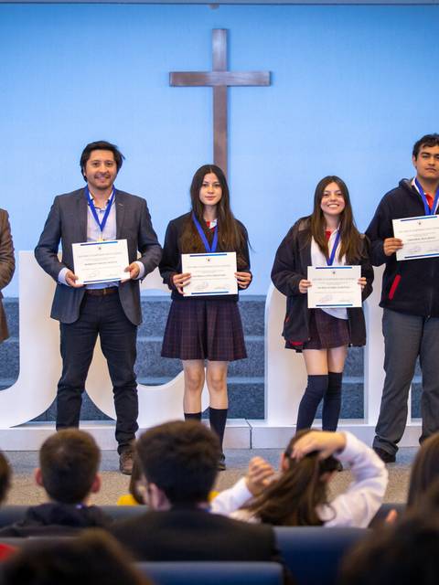 Un grupo de estudiantes se presenta en un escenario recibiendo diplomas en una ceremonia educativa.