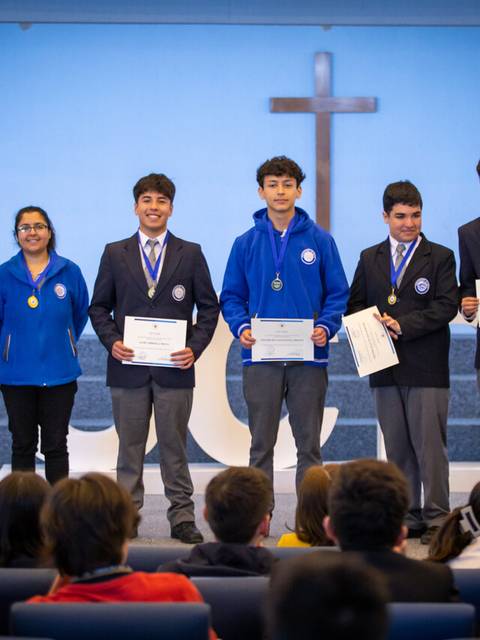 Un grupo de estudiantes en un evento de premiación con medallas y certificados en un escenario.