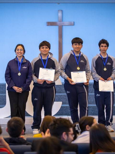 Un grupo de estudiantes recibe reconocimientos en un evento educativo frente a una cruz.