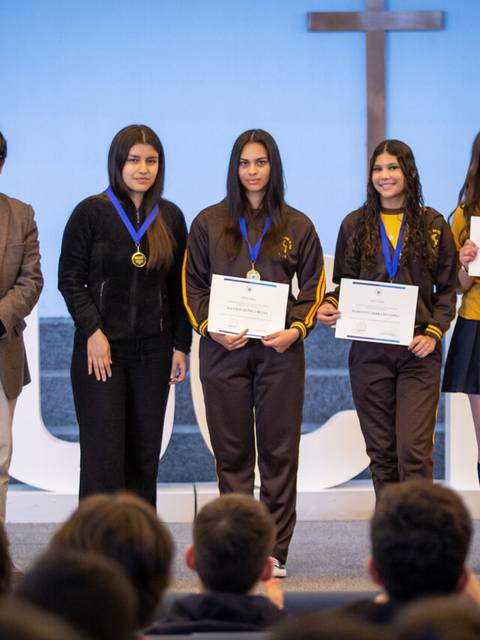 Cuatro jóvenes reciben certificados en una ceremonia escolar.
