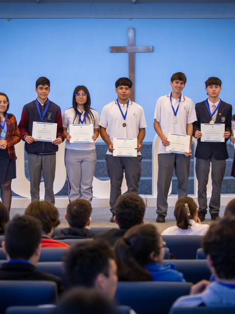 Un grupo de estudiantes orgullosos sostiene sus certificados y medallas en un evento de premiación en un auditorio.