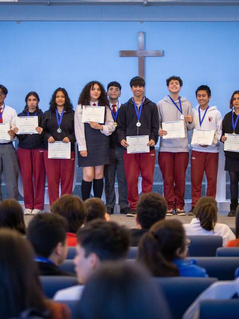 Un grupo de estudiantes en un escenario sonríen mientras sostienen certificados y medallas.