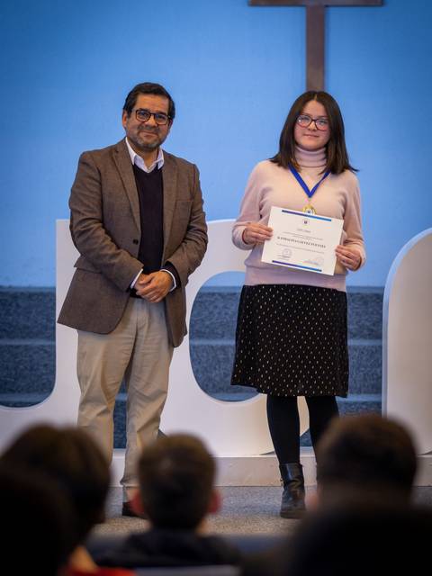 Una mujer joven sostiene un certificado mientras sonríe junto a un hombre en un evento de premiación.