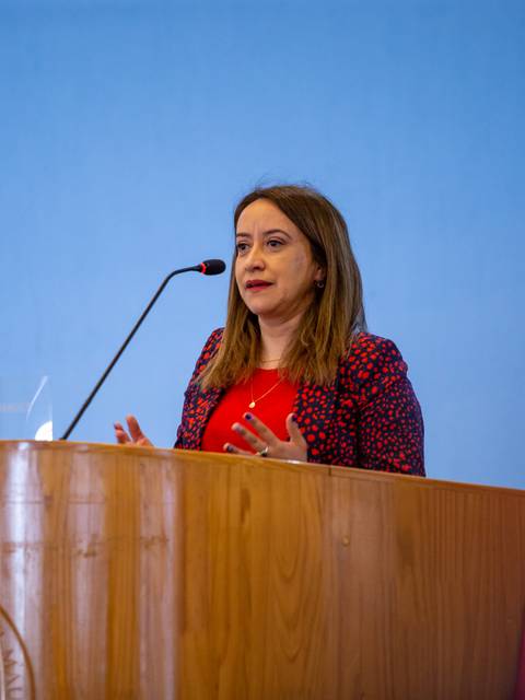 Una mujer está dando un discurso frente a un podio en un ambiente institucional.