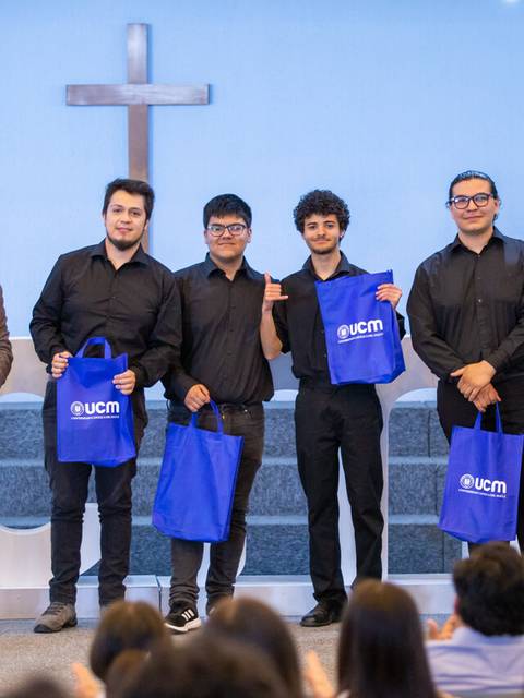 Un grupo de cinco personas en un evento, todas vestidas de negro, sosteniendo bolsas azules con el logo de ucm.