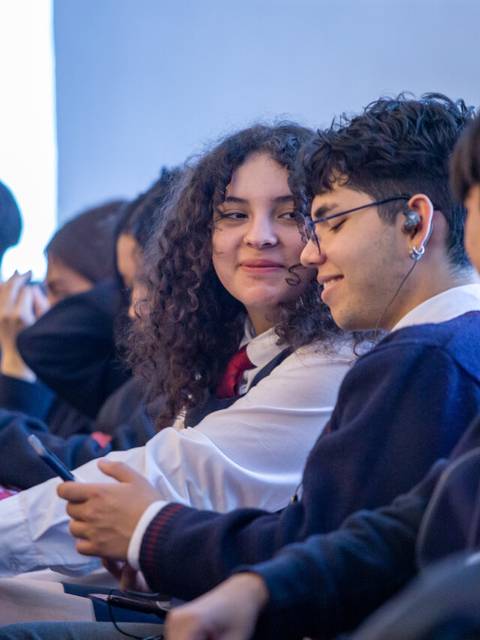 Un grupo de estudiantes conversando y sonriendo en un aula.