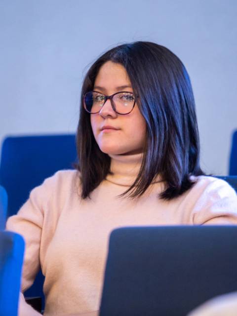 Una joven con gafas sentada en un auditorio, mirando fijamente al frente.