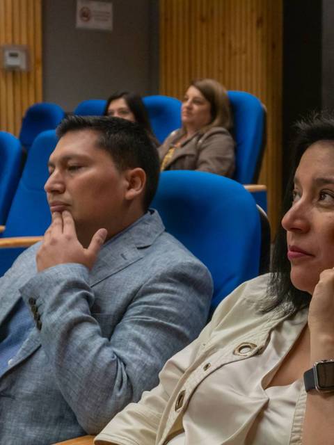 Un grupo de personas asiste a una presentación en un auditorio moderno con sillas azules.