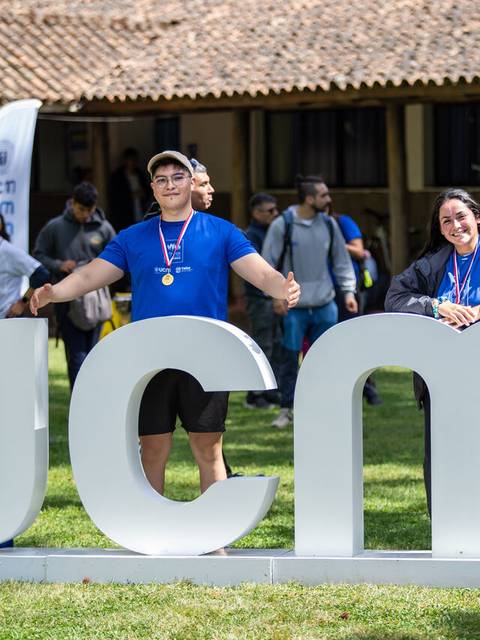 Un grupo de personas sonrientes posan junto a un letrero grande que dice 'UCM' en un evento al aire libre.