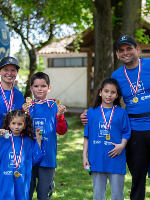 Un grupo de cuatro personas, entre adultos y niños, posan felices con medallas en un evento al aire libre.