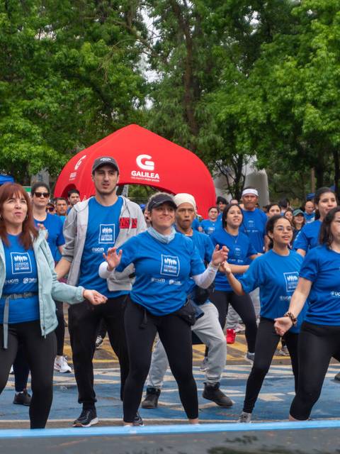 Un grupo de personas vestidas con camisetas azules se mueve en una actividad al aire libre rodeadas de árboles y carpas.