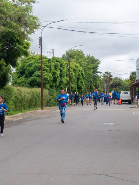 Un grupo de personas corre por una calle rodeada de árboles en un día nublado.