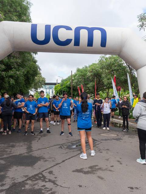 Un grupo de personas se prepara para participar en una carrera bajo un arco de meta con el logo de UCM.