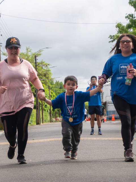 Tres personas corriendo en una carrera, dos adultos acompañan a un niño que lleva una medalla.