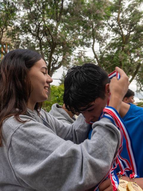 Una persona le coloca una medalla a otra en un evento deportivo.