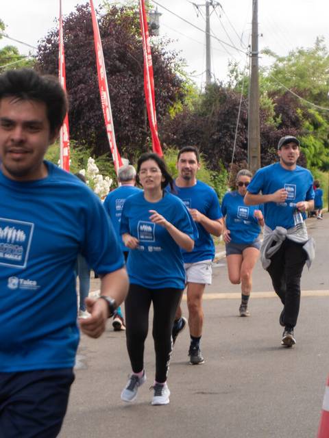 Un grupo de personas corre en una carrera al aire libre, vistiendo camisetas azules.