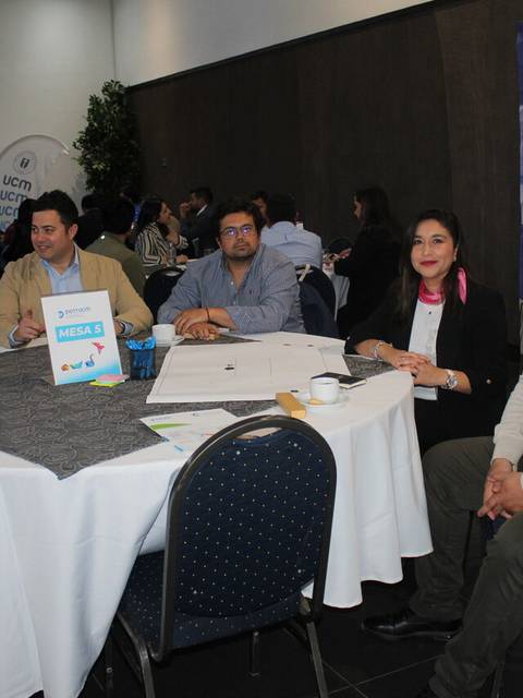 Grupo de personas sentadas alrededor de una mesa durante un evento en un salón.