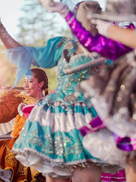 Un grupo de bailarinas en coloridos trajes realizan una coreografía en un escenario al aire libre.