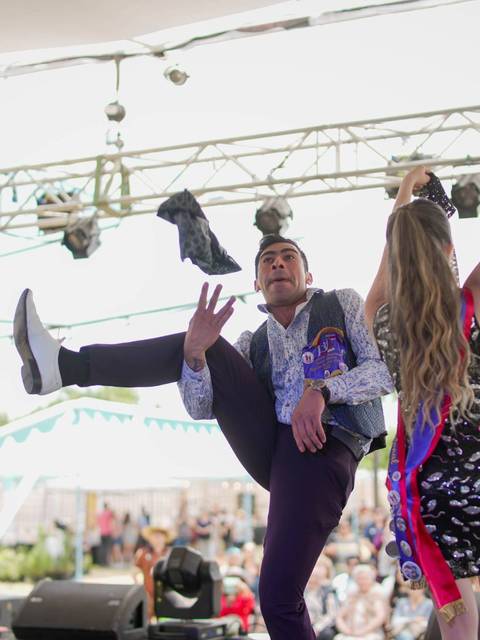 Un bailarín presenta una rutina en un escenario al aire libre mientras una mujer lo acompaña.