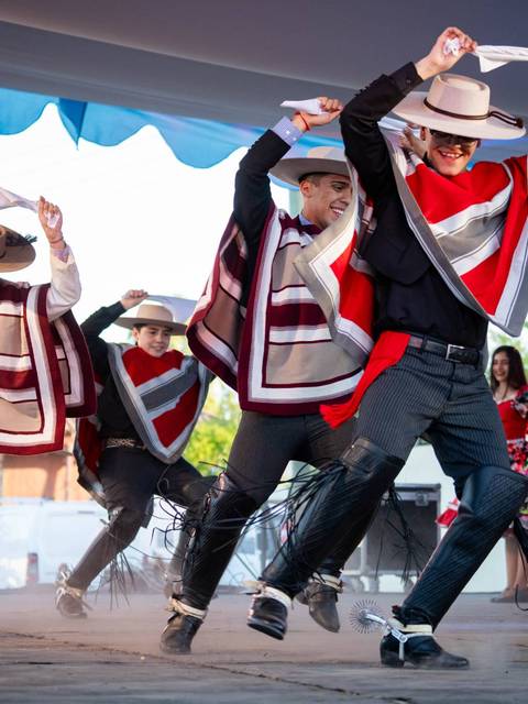 Un grupo de bailarines en trajes tradicionales realiza una danza folclórica en un escenario al aire libre.
