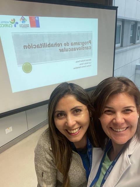 Dos mujeres sonrientes posando para una selfie en un entorno profesional.