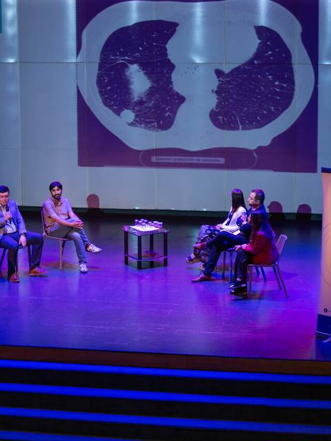 Una mesa redonda sobre temas relacionados con el cáncer, con varios expositores en un escenario iluminado.