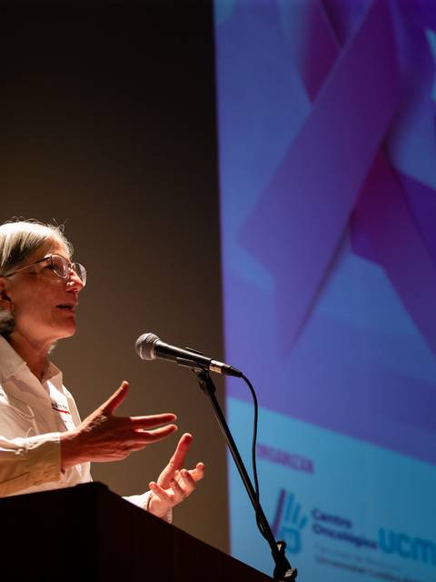 Una mujer está dando una charla en un evento sobre oncología.