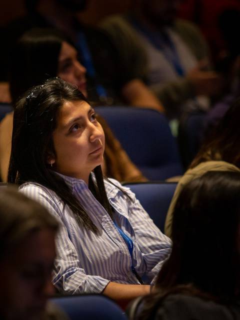 Una mujer observa detenidamente mientras asiste a un evento en un auditorio.