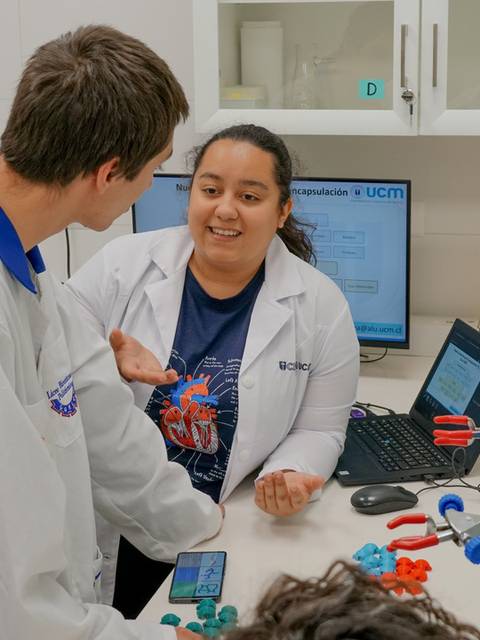 Estudiantes conversan en un laboratorio con equipos científicos presentes.