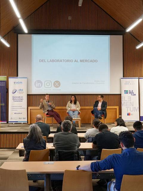 Un panel de discusión en un auditorio con varios asistentes y presentadores, enfocado en la temática de la transición del laboratorio al mercado.