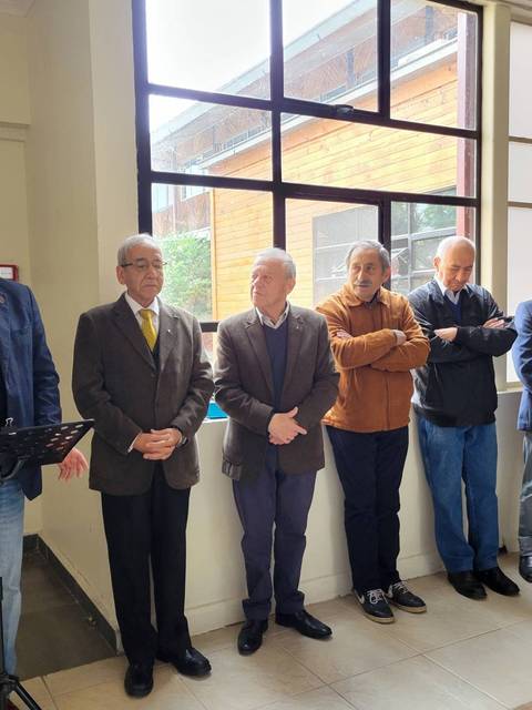 Un grupo de hombres de pie en un interior, mientras uno de ellos habla frente a un micrófono.