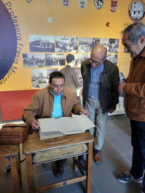 Tres hombres observan un libro en un entorno educativo.