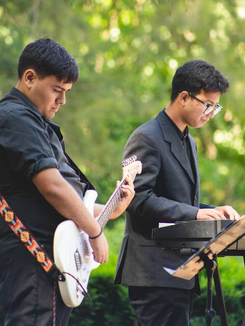 Dos jóvenes músicos tocan instrumentos en un entorno al aire libre.
