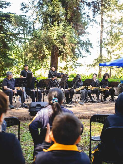 Una banda de música se presenta frente a un público en un parque al aire libre.