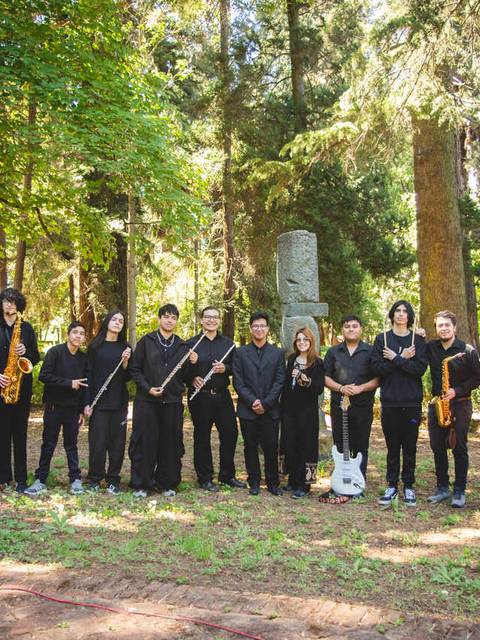 Un grupo de músicos posando en un bosque con instrumentos musicales.
