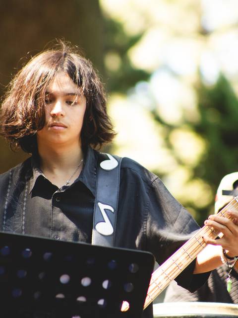 Un joven toca el bajo en un ambiente al aire libre durante un evento musical.