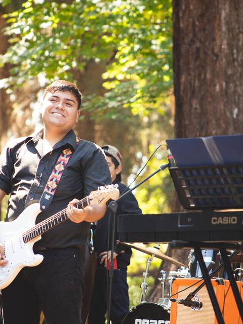 Un grupo de jóvenes músicos actúa al aire libre, con guitarras y un teclado, en medio de un entorno natural.