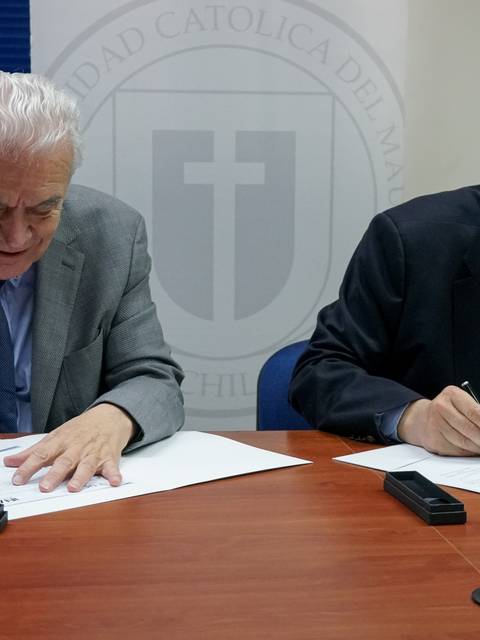 Dos hombres mayores firmando documentos en una mesa.