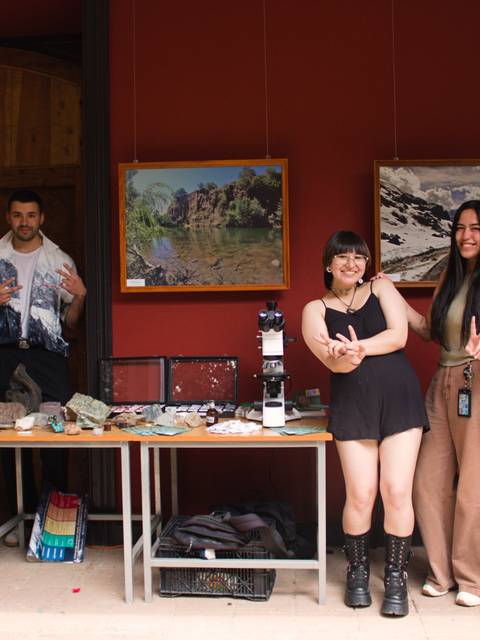Un grupo de cinco jóvenes posando frente a una exhibición artística en un ambiente acogedor.
