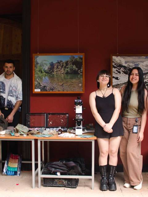 Un grupo de cinco personas posan frente a una exposición de arte con varias obras en las paredes.